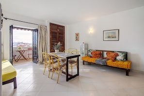 Un salon comprenant une table à manger, des chaises, un canapé et une vue sur l’extérieur grâce à une porte ouverte.