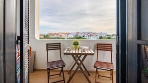 Ein Balkon mit Tisch und zwei Stühlen, einer Topfpflanze und Blick auf Gebäude.