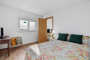 Une chambre à coucher comprenant un lit, une armoire en bois, un bureau avec une chaise, une fenêtre et un téléviseur.