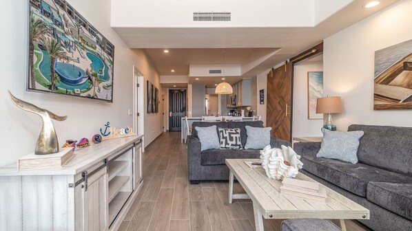 A modern living room with a grey sofa, a wooden coffee table, and a dining area in the background. - Las Palomas Beach and Golf Resort (Puerto Peñasco)