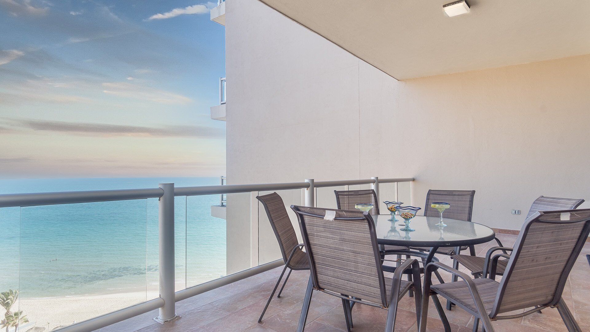 Un balcon avec une table et des chaises, donnant sur une plage et la mer.