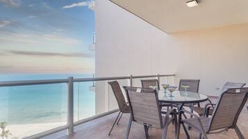 Un balcon avec une table et des chaises, donnant sur une plage et la mer.