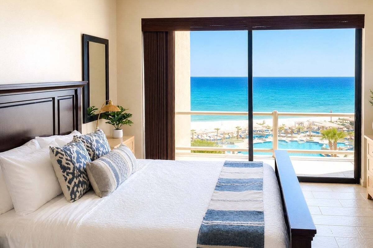 Habitación de hotel con cama, un banco, vista al océano y zona de piscina.