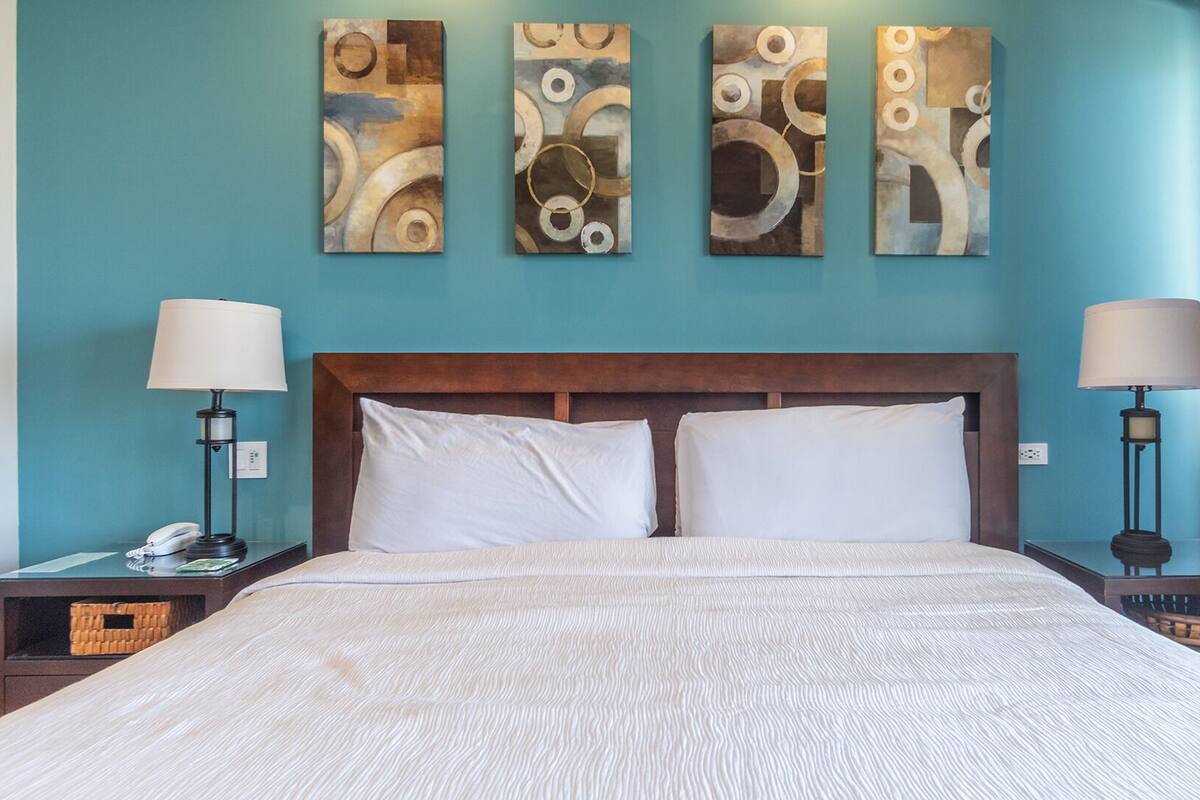 Una habitación de hotel con una cama grande, dos mesitas de noche, una lámpara y arte abstracto en la pared.