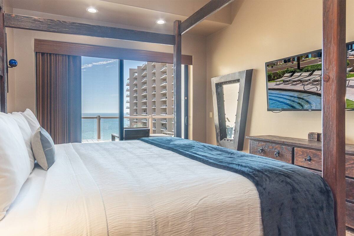 Habitación de hotel con una cama grande, vistas al mar y un balcón con piscina.