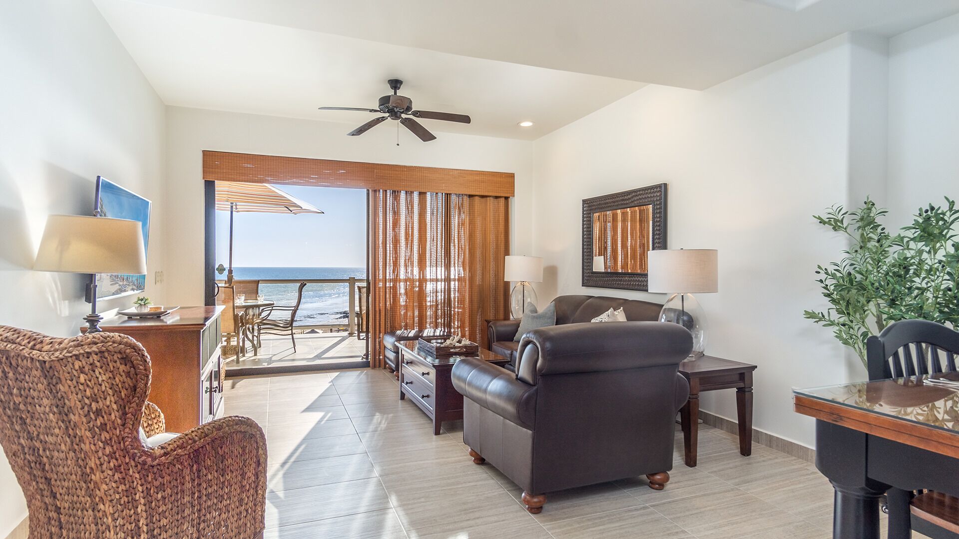 A spacious living area with a view of the ocean, a ceiling fan, and a dining table with chairs.