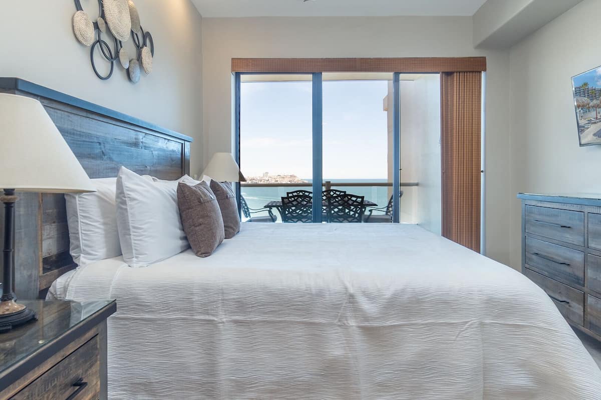 Un dormitorio con una cama grande, una mesita de noche, un aparador y vistas al mar a través de una puerta corrediza.