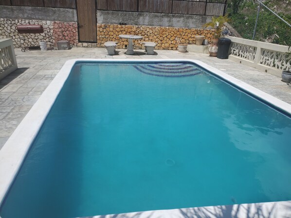A rectangular swimming pool with a stone wall and a wooden fence in the background. - BAYVIEW LUXURY RETREATS   (Reading)