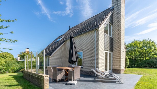 Une maison moderne dotée d’un patio comprenant une table à manger, des chaises et un parasol.