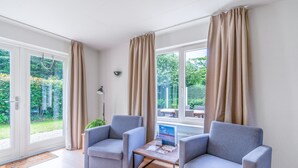 Une pièce moderne avec deux fauteuils gris, une petite table et une vue sur un jardin, grâce à de grandes fenêtres.