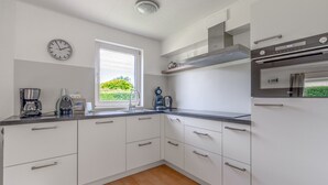 Une cuisine moderne avec des meubles blancs, un four encastré et une fenêtre donnant sur un paysage verdoyant.