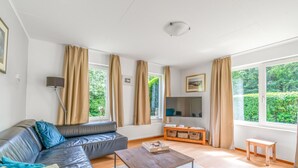 Un salon moderne avec un canapé en cuir, une table basse en bois, un téléviseur et de grandes fenêtres dotées de rideaux.