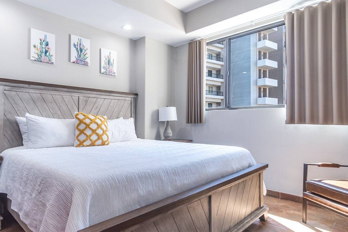Quarto de hotel com uma cama grande, cabeceira de madeira e obras de arte nas paredes.