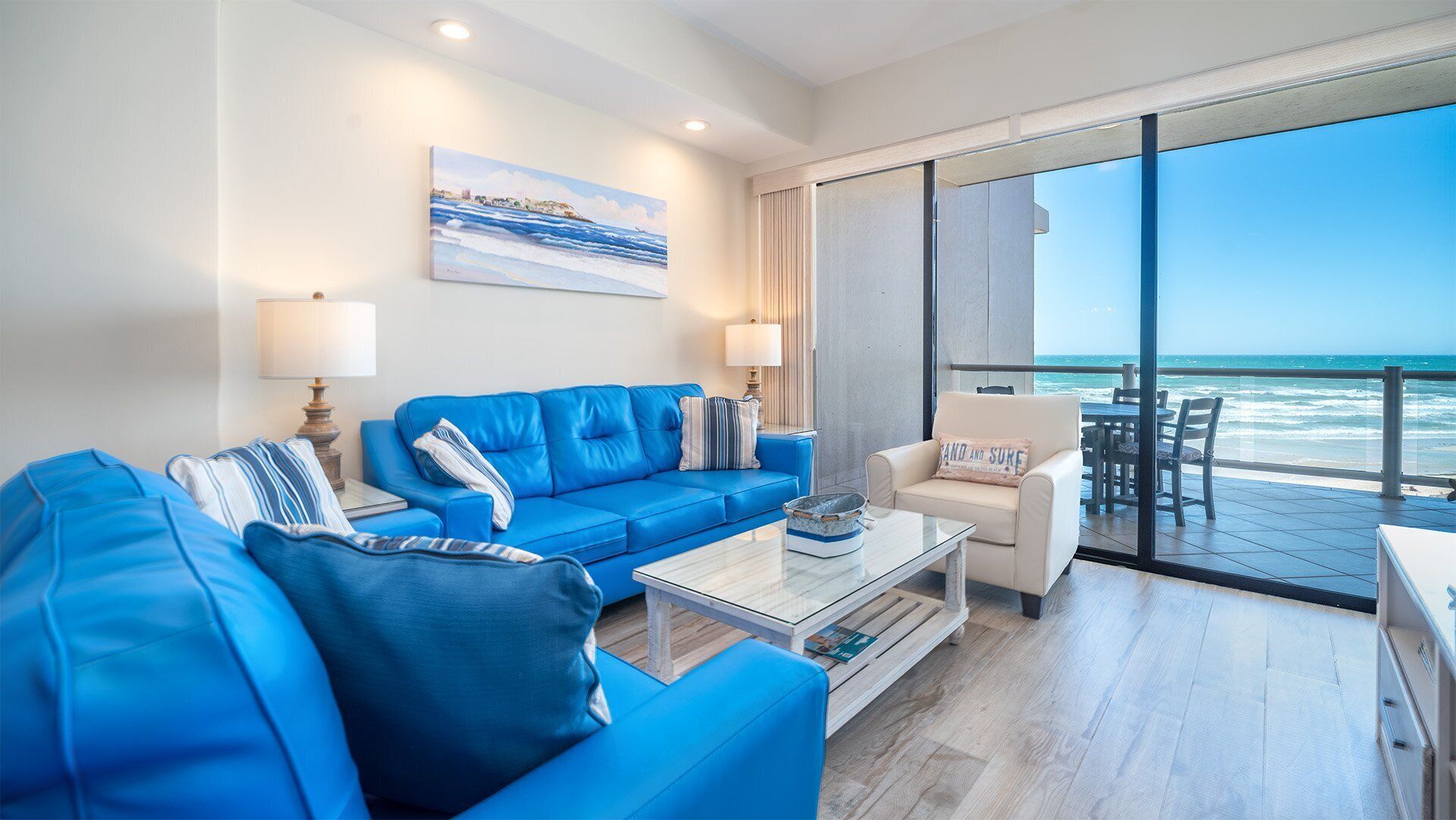 Ein modernes Wohnzimmer mit einem blauen Sofa, einem Couchtisch und Blick auf das Meer durch große Fenster.