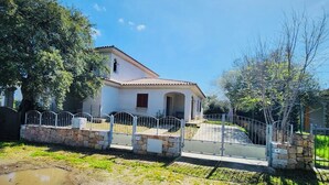 A single-story house with a tiled roof, a stone wall in front, and a metal fence. - Casa Vacanza Salix (San Teodoro)