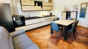 A modern kitchen with wooden cabinets, a dining table with chairs, and a grey sofa. - Casa Vacanza Salix (San Teodoro)