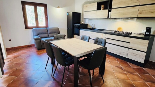 A compact kitchen with a dining area, featuring a tiled floor, a built-in stove, and wooden cabinets. - Casa Vacanza Salix (San Teodoro)