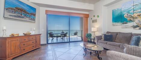 A spacious living room with a large glass door leading to a balcony, a wooden cabinet, a glass coffee table, and a grey sofa.