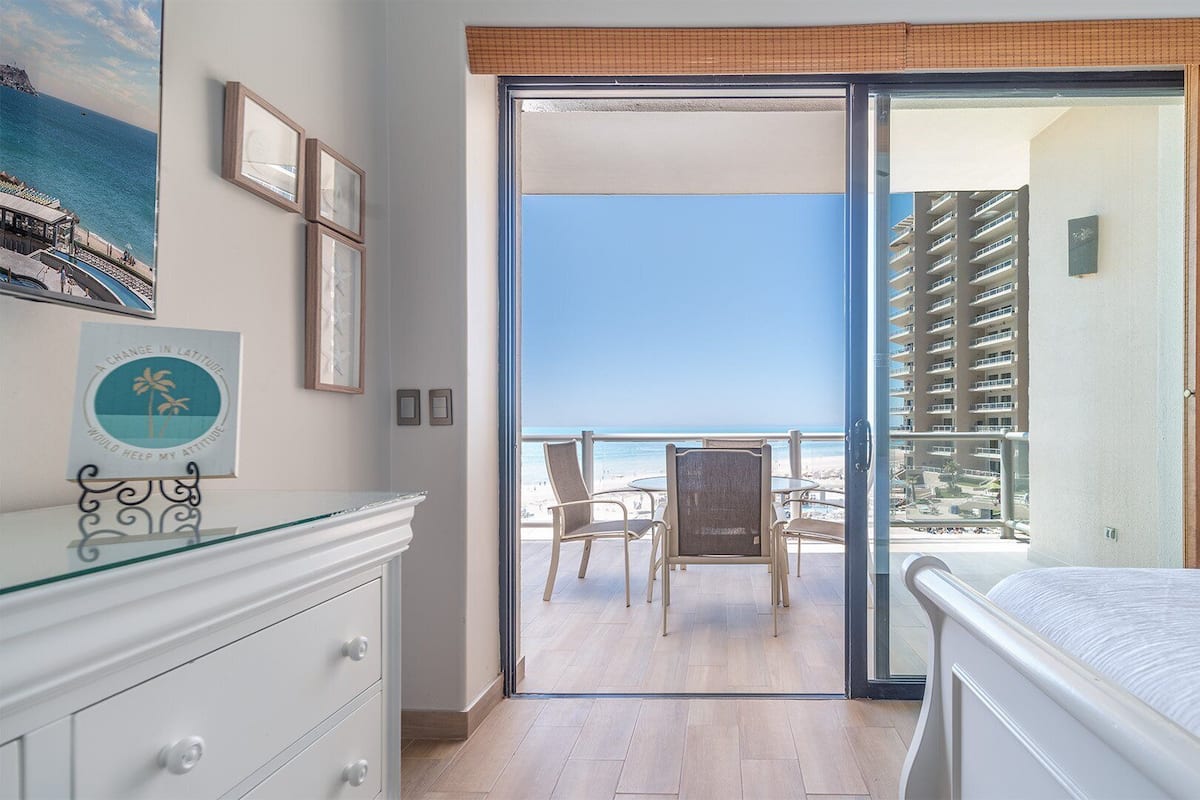 Een hotelkamer met balkon, een bed, een dressoir en uitzicht op strand en zee.