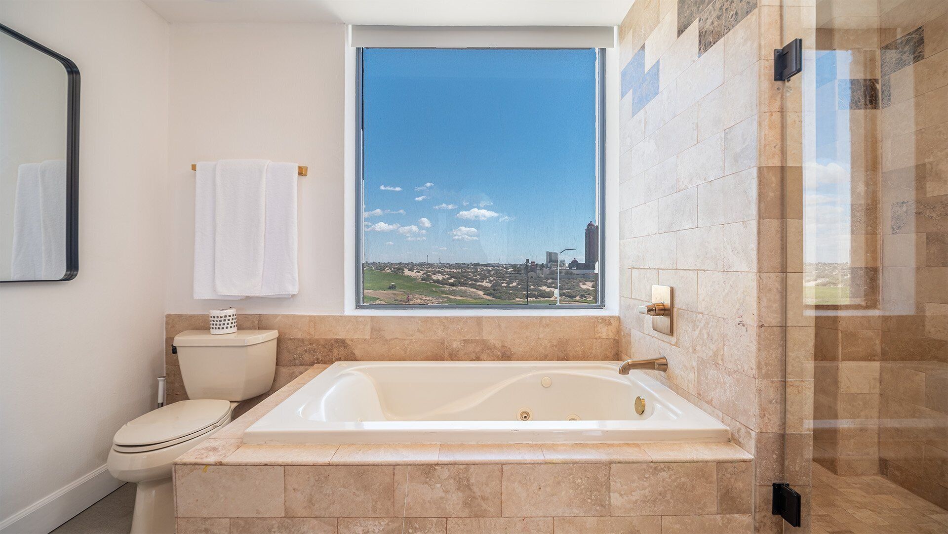 A bathroom with a large bathtub, a toilet, and a window offering a city view.