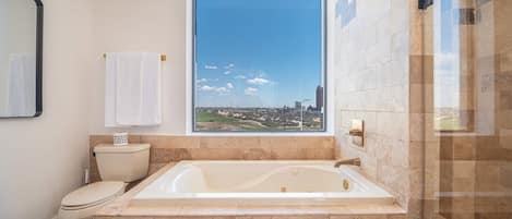 A bathroom with a large bathtub, a toilet, and a window offering a city view.