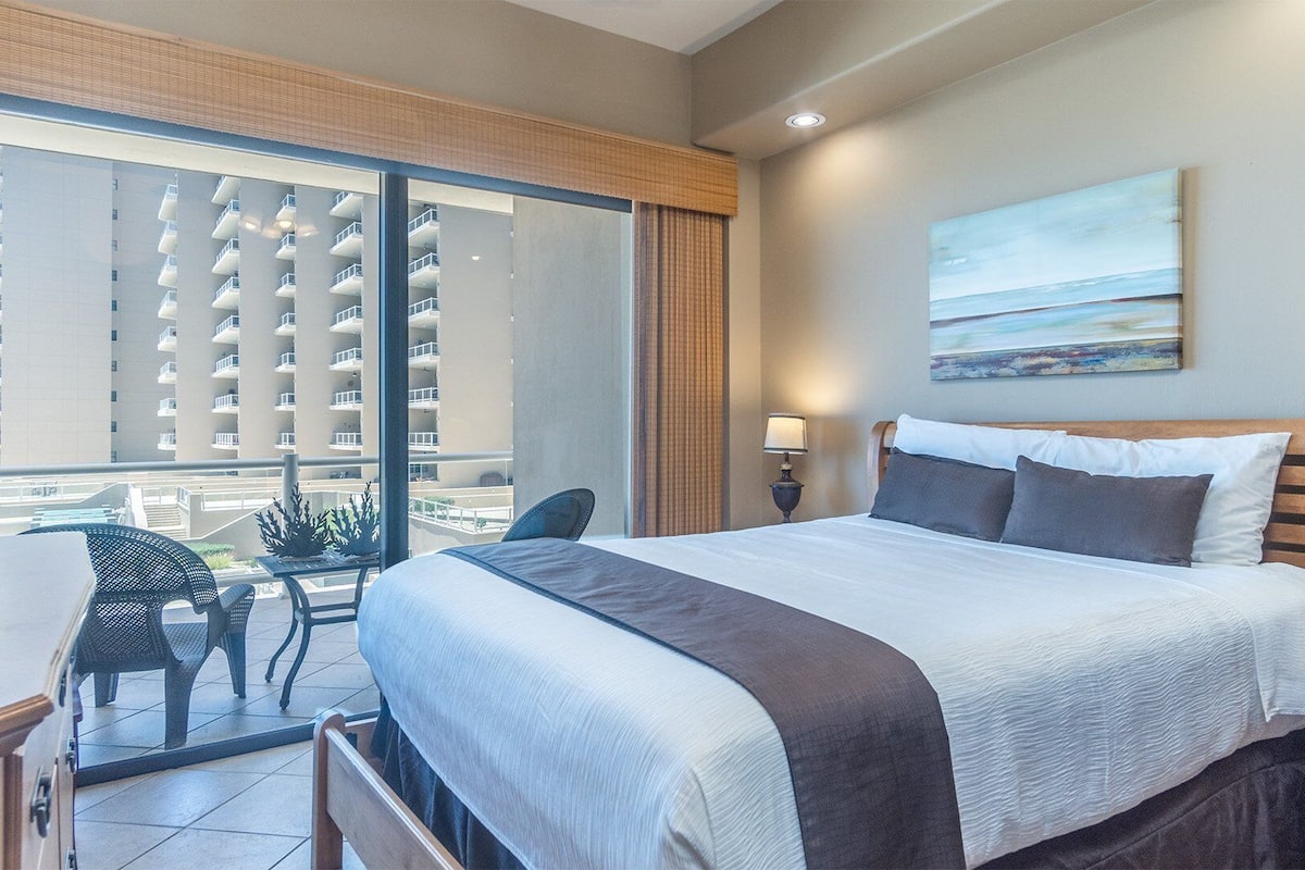 Hotelkamer met een groot bed, een bureau, een stoel, een lamp en uitzicht op een hoog gebouw.