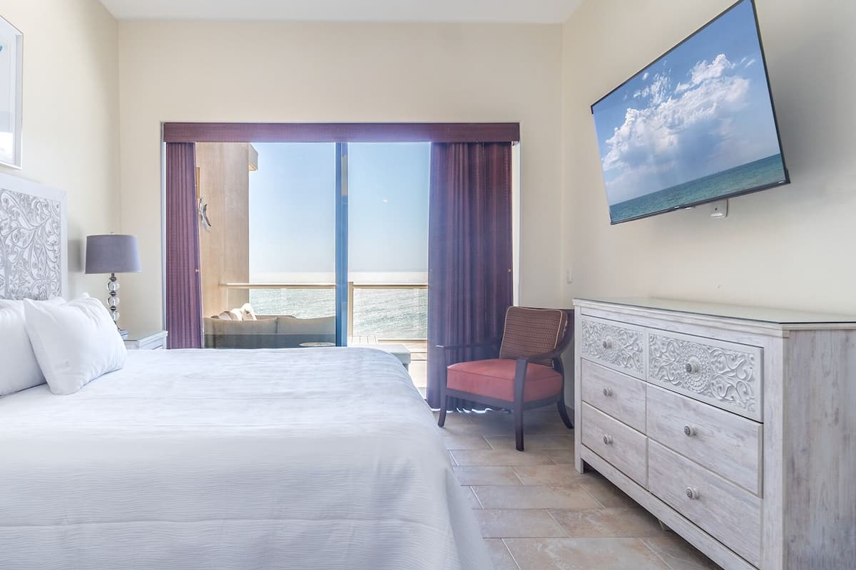 Een hotelkamer met een groot bed, een stoel, een dressoir en een televisie aan de muur.