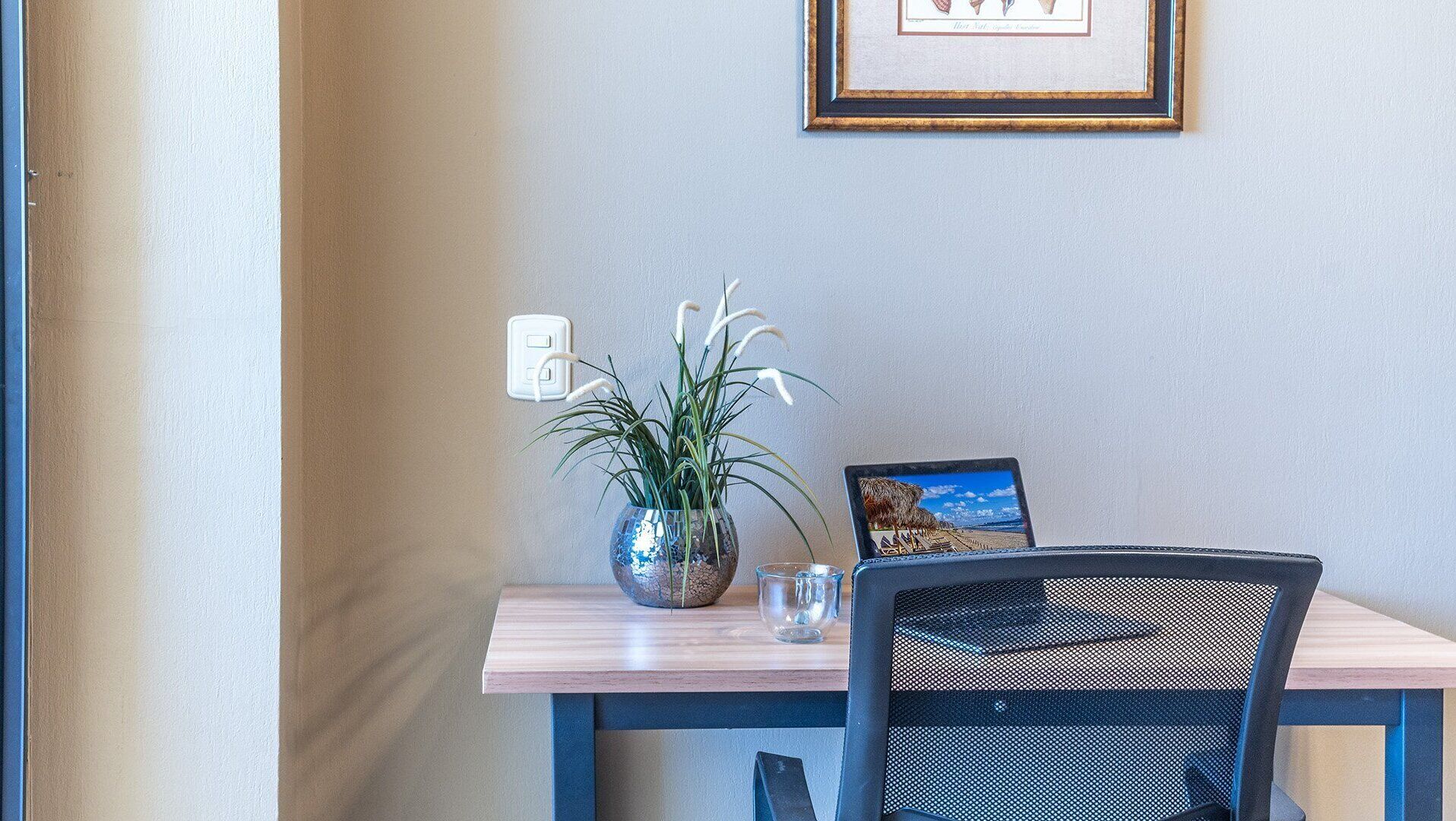 A dining area with a table, chairs, a vase with a plant, a framed picture, and a wall socket.