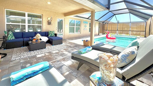 Ein überdachter Außenbereich mit Pool, Liegestühlen und einer Sitzecke mit Sofa und Tisch.