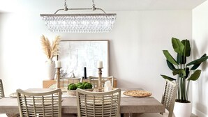 Ein Essbereich mit Holztisch, Korbstühlen, einer Chandelier und einem Blumentopf.