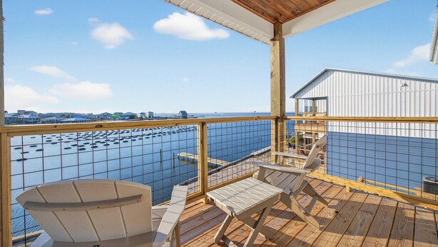 Eine Holzterrasse mit Blick auf Wasser und Boote, ein überdachter Bereich mit Geländer sowie ein Gebäude im Hintergrund.