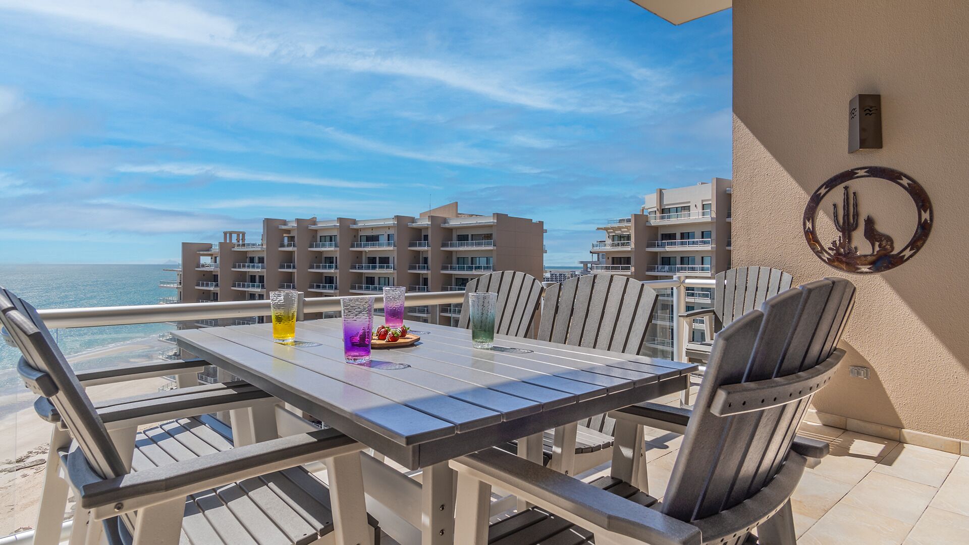 Un balcone con tavolo e sedie, affacciato su una spiaggia e degli edifici.