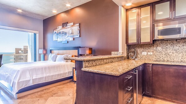 Une chambre d’hôtel moderne équipée d’un lit, d’une petite kitchenette et offrant une vue sur l’océan.