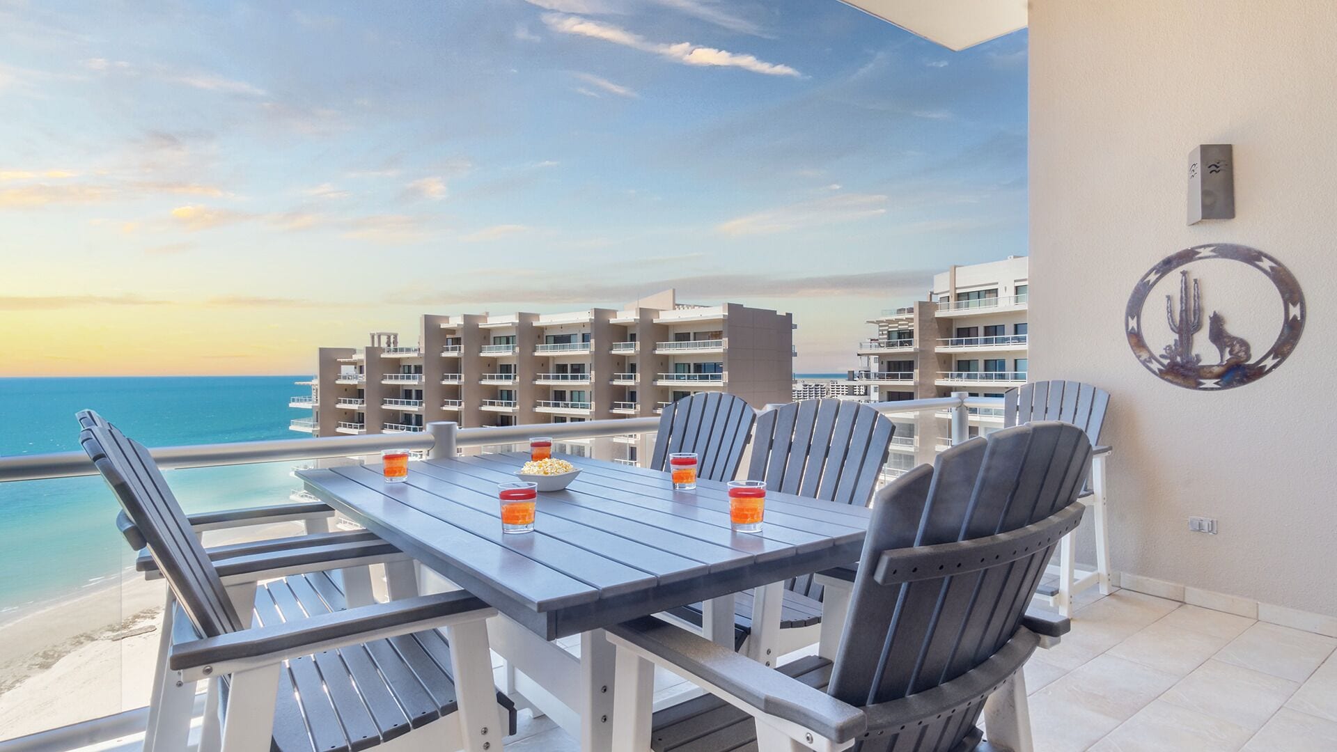 A balcony with a table and chairs overlooking the ocean, with buildings in the background.