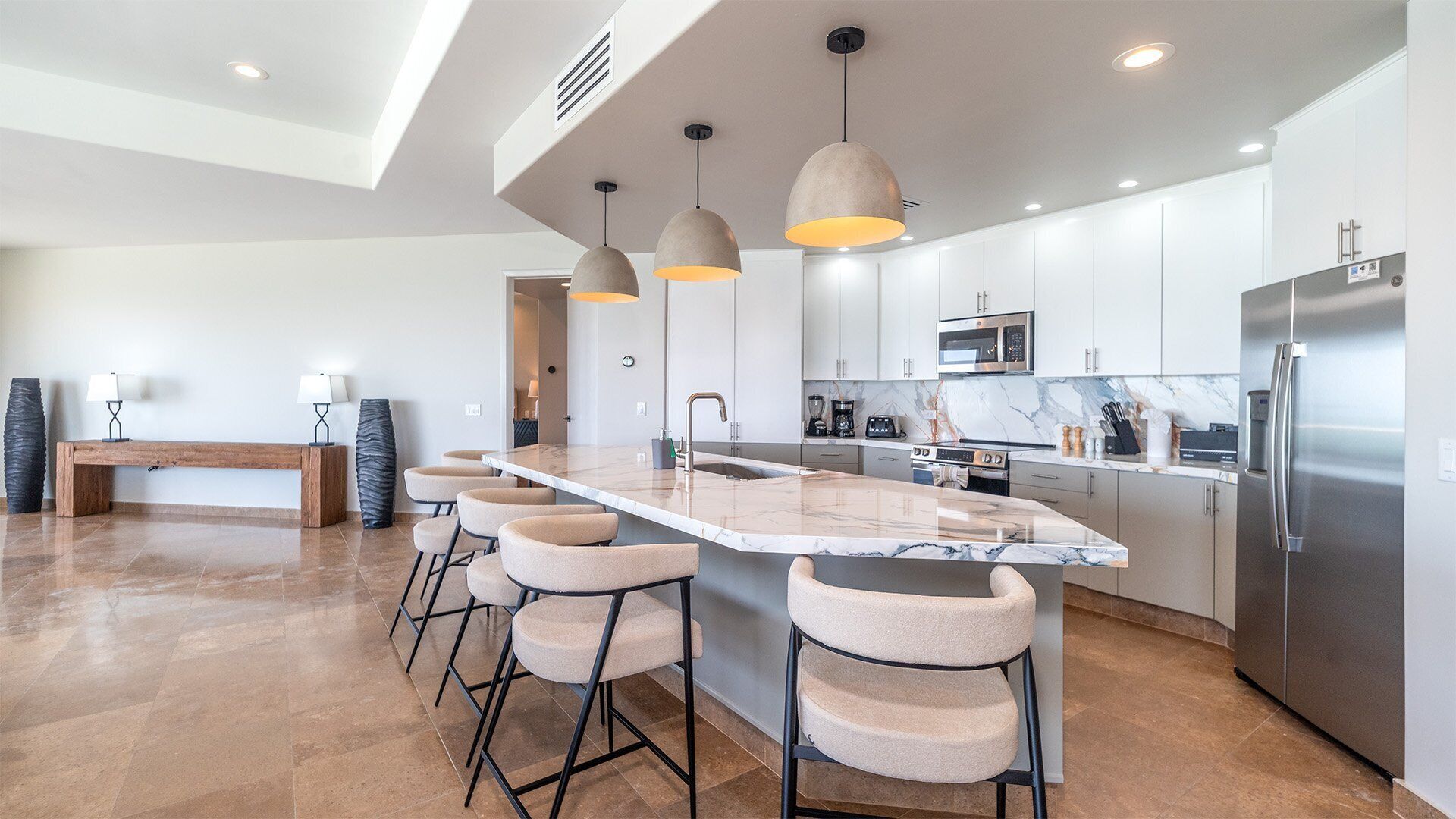 Una cocina moderna con una isla central, taburetes de bar, electrodomésticos de acero inoxidable e iluminación colgante.