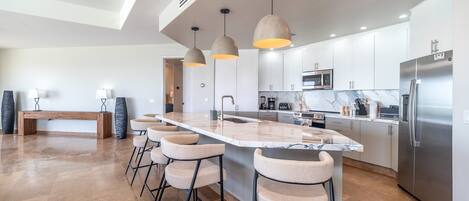 Una cocina moderna con una isla central, taburetes de bar, electrodomésticos de acero inoxidable e iluminación colgante.