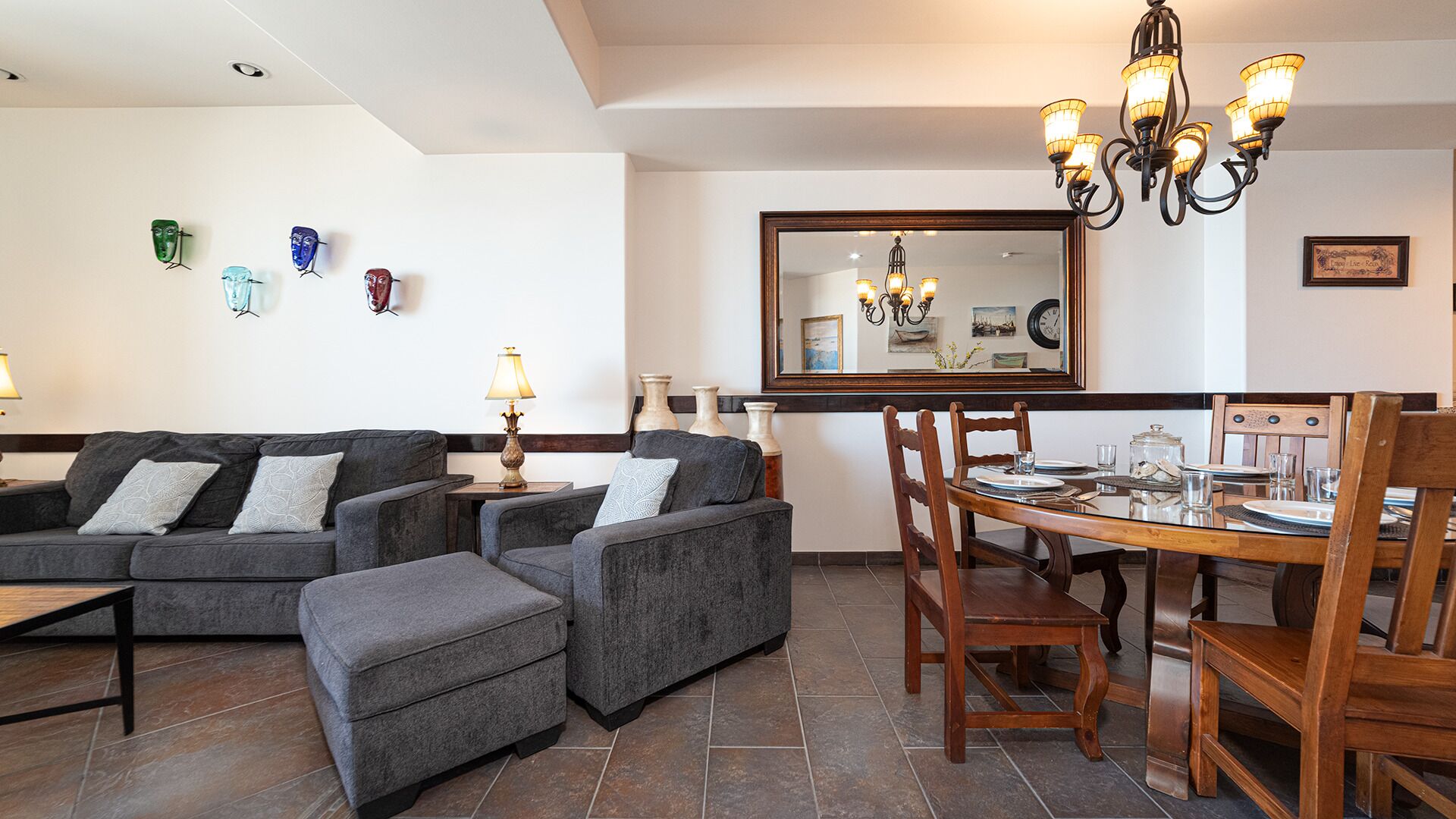 A dining area with a wooden table and chairs, a sofa set, and a chandelier.