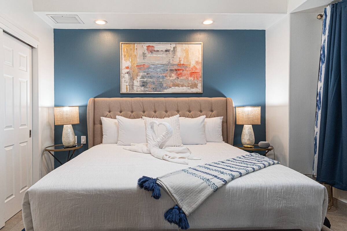 Une chambre à coucher avec un grand lit, deux tables de chevet, une tête de lit, un tableau au mur et une porte.