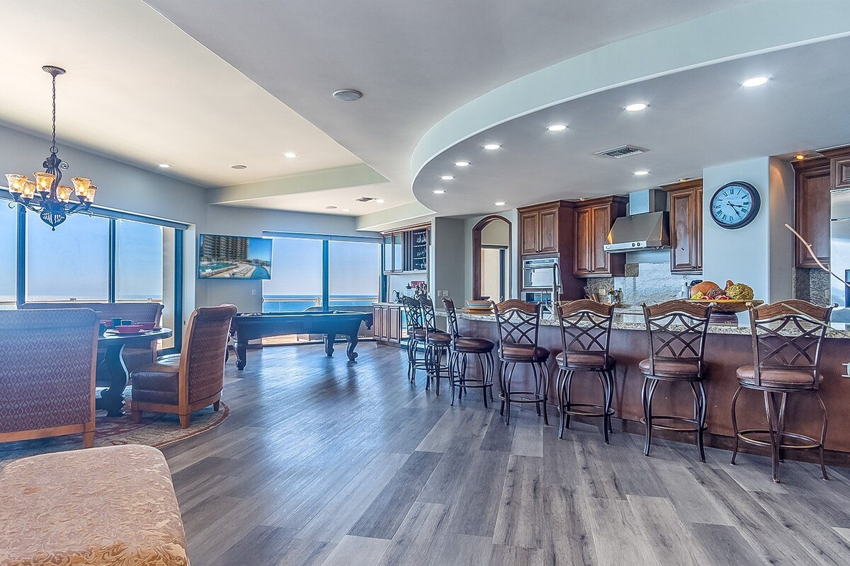 A spacious kitchen with a bar area, large windows, and a pool table.