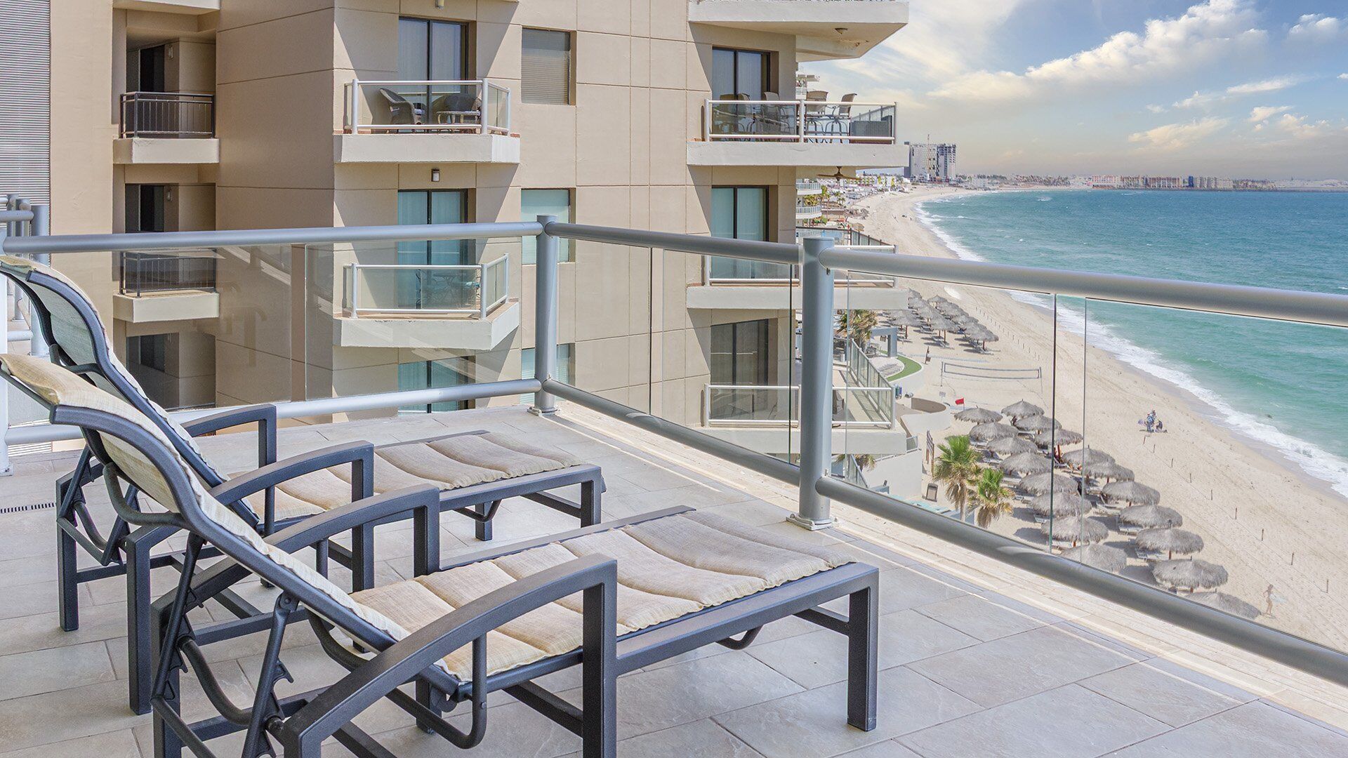 A balcony with lounge chairs overlooking a beach and ocean.