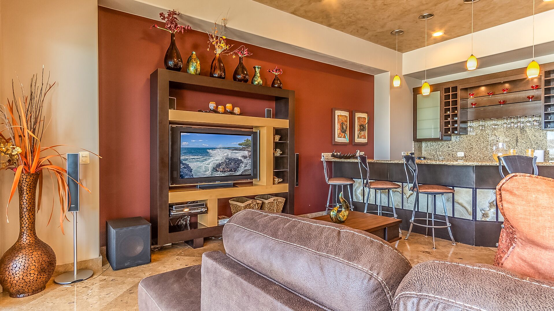 A modern living room with a large flat-screen TV, comfortable seating, a bar area, and decorative vases.