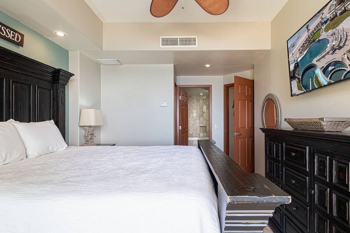 Une chambre à coucher avec un grand lit, une commode, une lampe et un tableau représentant une piscine.