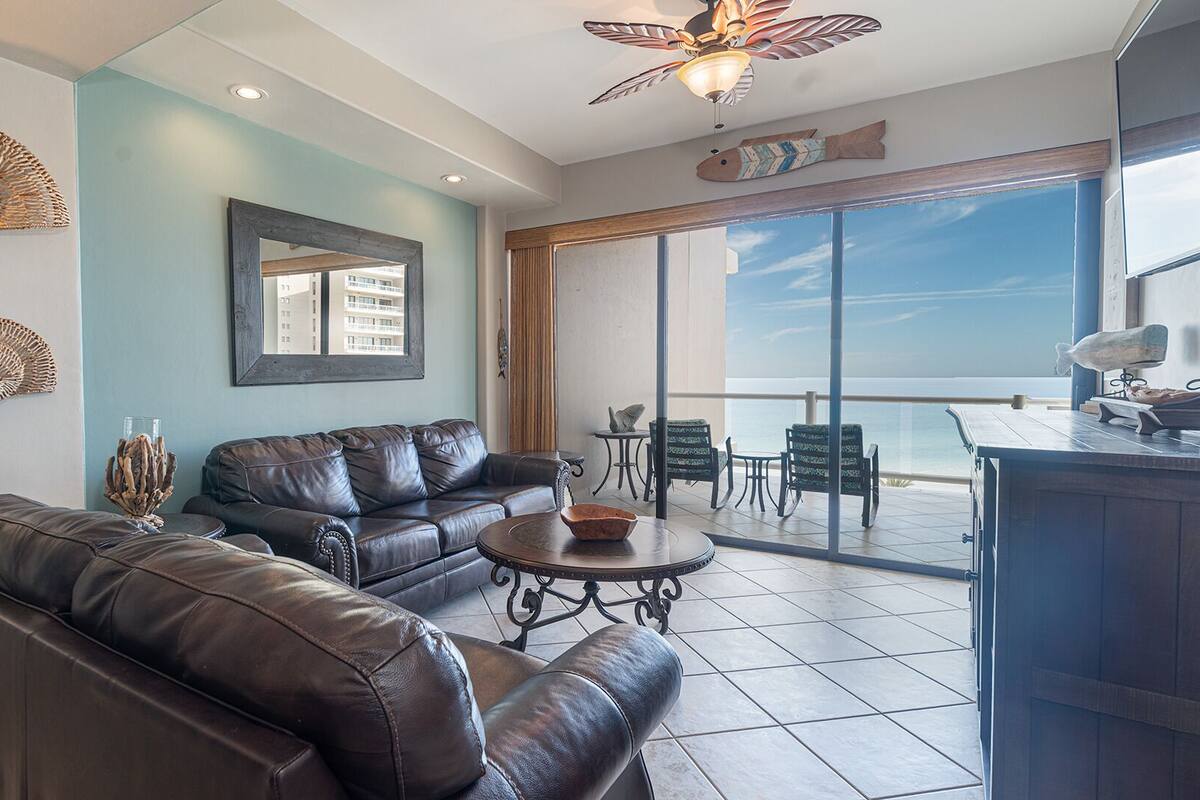 A spacious living area with a leather sofa, a coffee table, and a balcony with a view of the sea.
