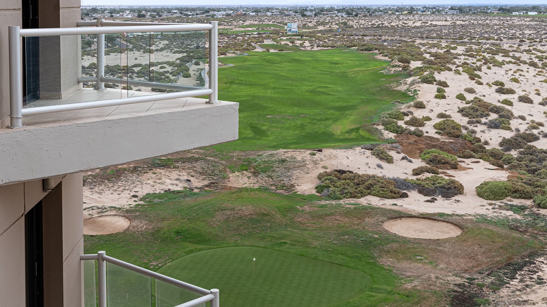 A view of a golf course from a high vantage point, including a building with a balcony overlooking the course.