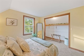Une chambre à coucher comprenant un lit, une fenêtre, un miroir, un étendoir et une porte donnant sur une autre pièce.