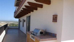 An outdoor kitchen area with a grill and a small table, a wooden pergola, and a view of the landscape. - 3-bedroom Ocean Front PENTHOUSE in marvelous Cabo San Lucas (Cabo San Lucas)