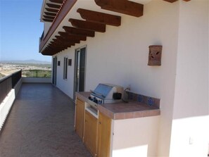 Un área de cocina al aire libre con una parrilla y una pequeña mesa, una pérgola de madera y vistas al paisaje.