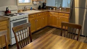 A compact kitchen with wooden cabinets, a stainless steel refrigerator, and a dining table with chairs.