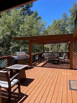Eine Holzterrasse mit Gartenmöbeln, darunter ein Tisch, Stühle und ein Grill.