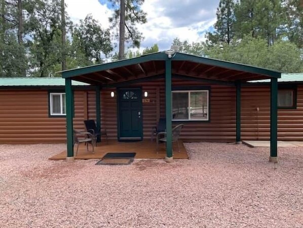 Eine Blockhütte mit überdachter Veranda, zwei Stühlen und einer Tür.